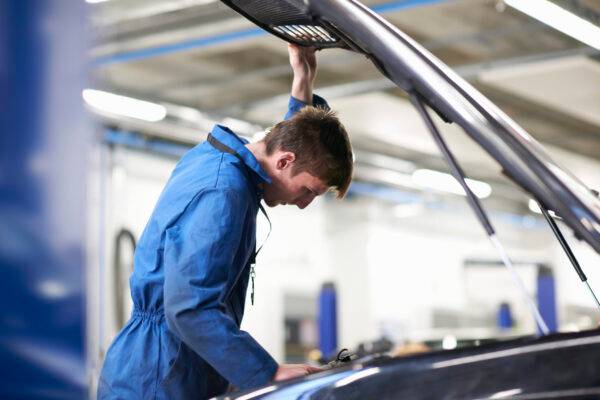 College mechanic student inspecting under car hood in repair garage